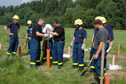 THW-Mitarbeiter in Arbeitskleidung und phosporeszierenden Helmen bereiten die in die Erde eingegrabenen R&ouml;hren f&uuml;r den Sprengstoff.